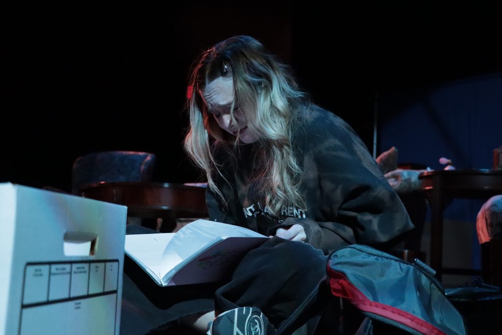 An actor sits on the ground, reading a book in distress.