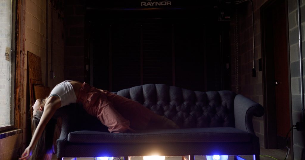 A dancer stretches out lengthwise over the edge of a couch.