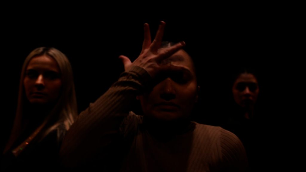 Three dancers from the shoulders up and dimly lit.